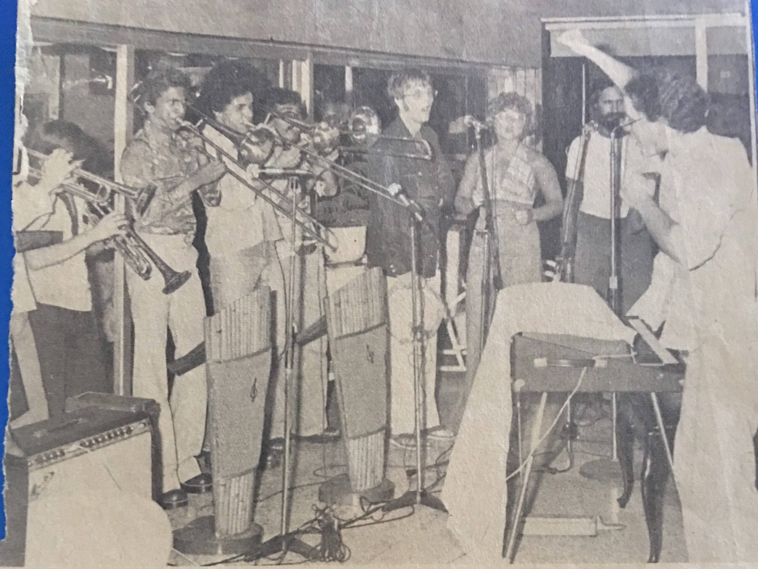 A lively jazz band performs on stage, featuring musicians playing brass instruments, with one conducting passionately. The scene captures the energy of a live musical event.