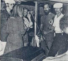 A group of musicians performing on stage, featuring a female vocalist with a microphone. The scene captures the energy of a live music event.