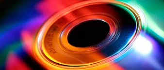 Close-up of a colorful CD, showcasing vibrant reflections and light patterns. The image emphasizes the disc's surface texture and artistic flair.